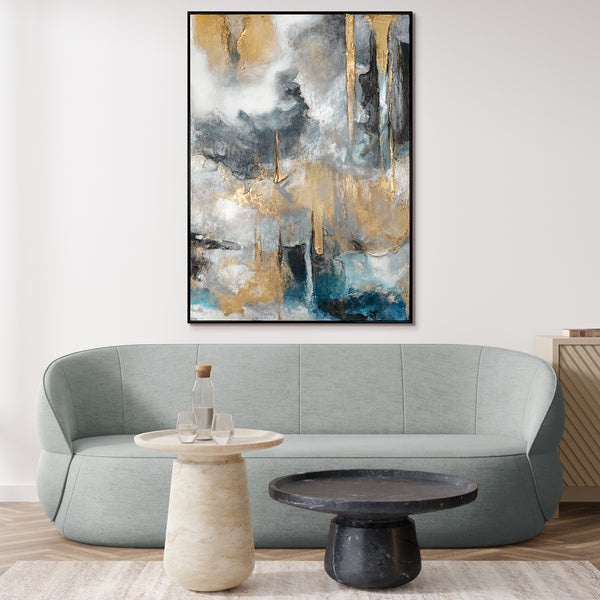 Modern abstract canvas painting in a black frame displayed above a light gray curved sofa in a minimalist room setting with a marble table and dark round coffee table